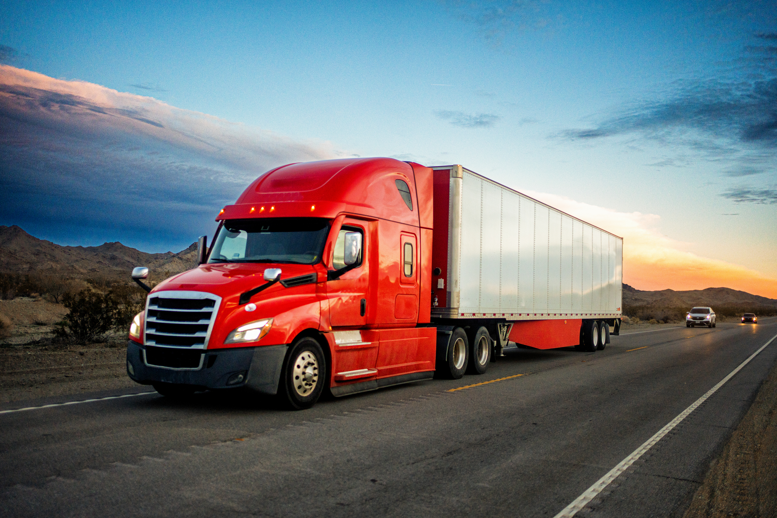 Red tractor trailer on the highway at dusk.